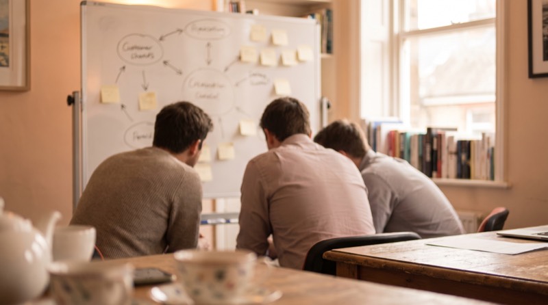 Colleagues at a whiteboard covered in hand-drawn diagrams and sticky notes