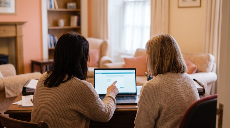 One person pointing at a laptop screen while explaining it to a colleague