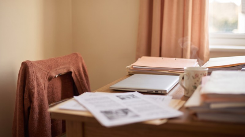An untidy desk of paper folders and loose printed spreadsheets beside a closed laptop